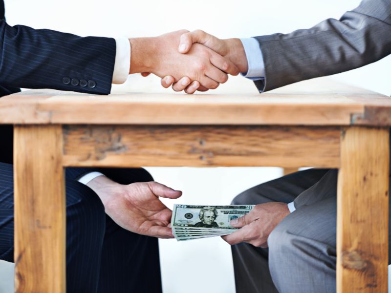 Employees shaking hands while money passes hands under a table.